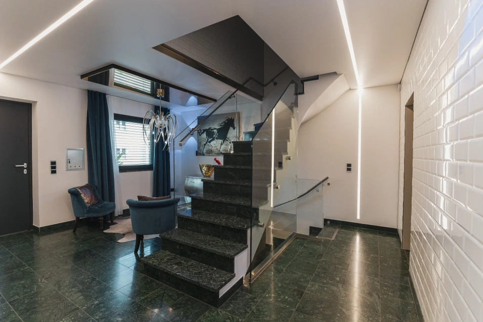 Bild vom Eingangsbereich. Auch hier dunkel-grünlicher Marmoroptik Boden mit einer Treppe nach oben und nach unten. Die Geländer sind aus Glas.