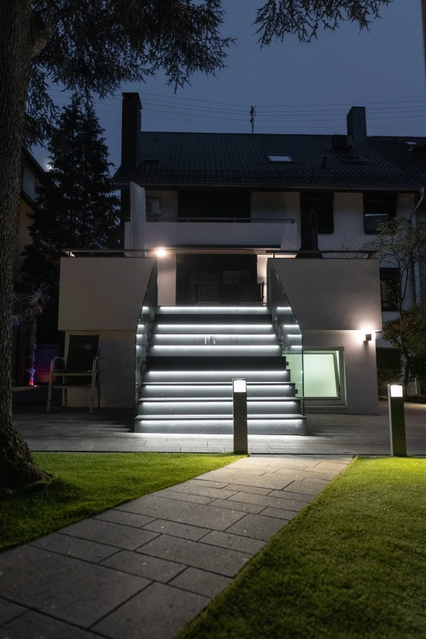 Das Bild zeigt das Haus von hinten. Der Garten ist beleuchtet. Eine Treppe führt hoch zu der Terrasse, mit dem Terrassenkamin.