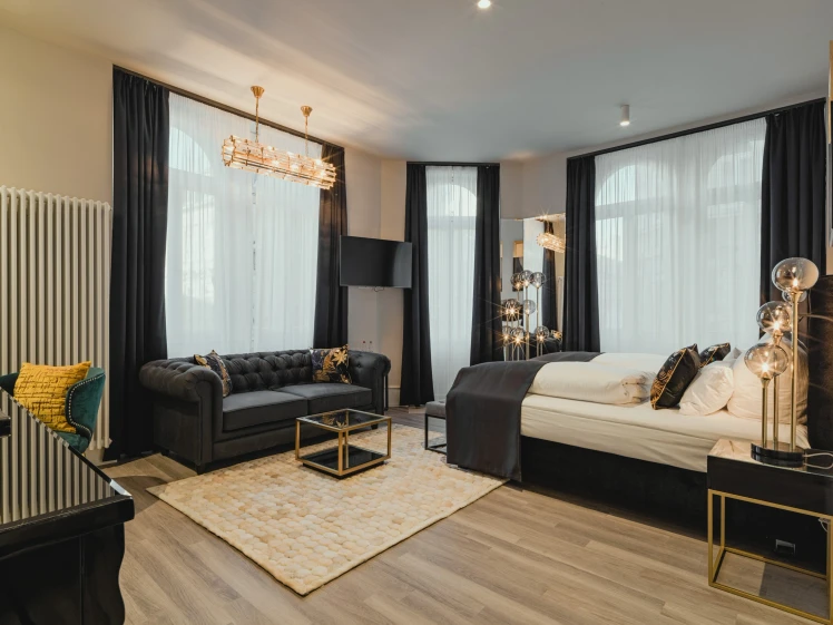Superior Room im BS Boutique Hotel Heidelberg. Mit einem schwarzen Bett, schwarzem Sofa und weißen Gardienen im Hotelzimmer.